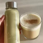 Homemade pistachio milk in a glass with a handful of pistachios beside it.